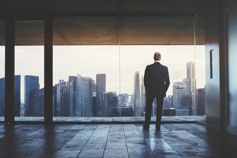 Man staring out floor to ceiling windows looking at a city skyline