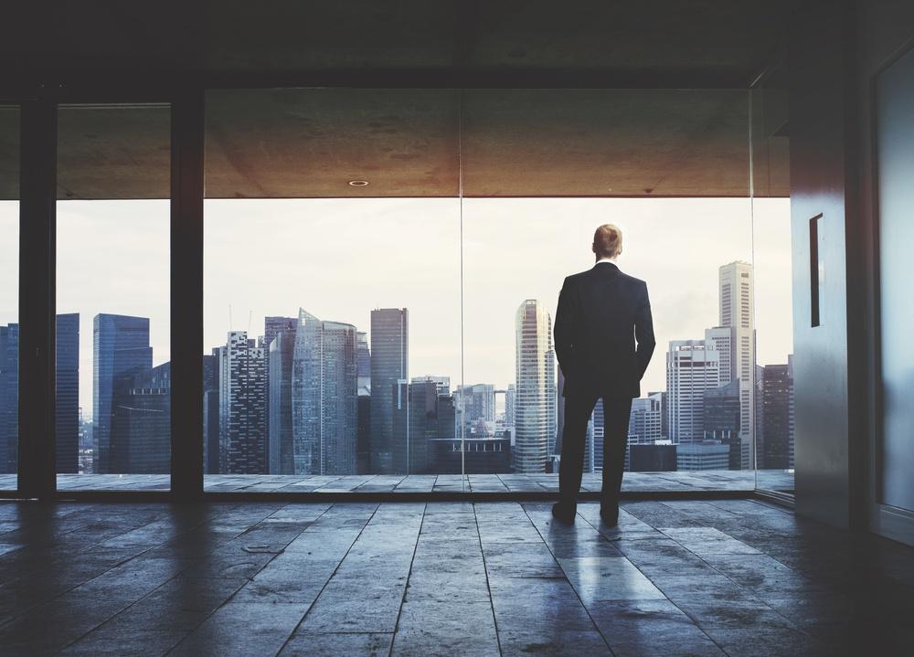 Man staring out floor to ceiling windows looking at a city skyline