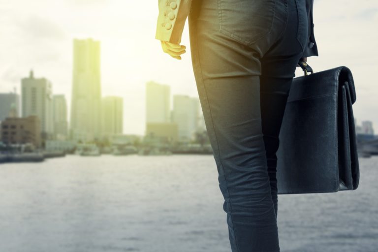 Close up of a person holding a briefcase in front of a harbor with a city in the background
