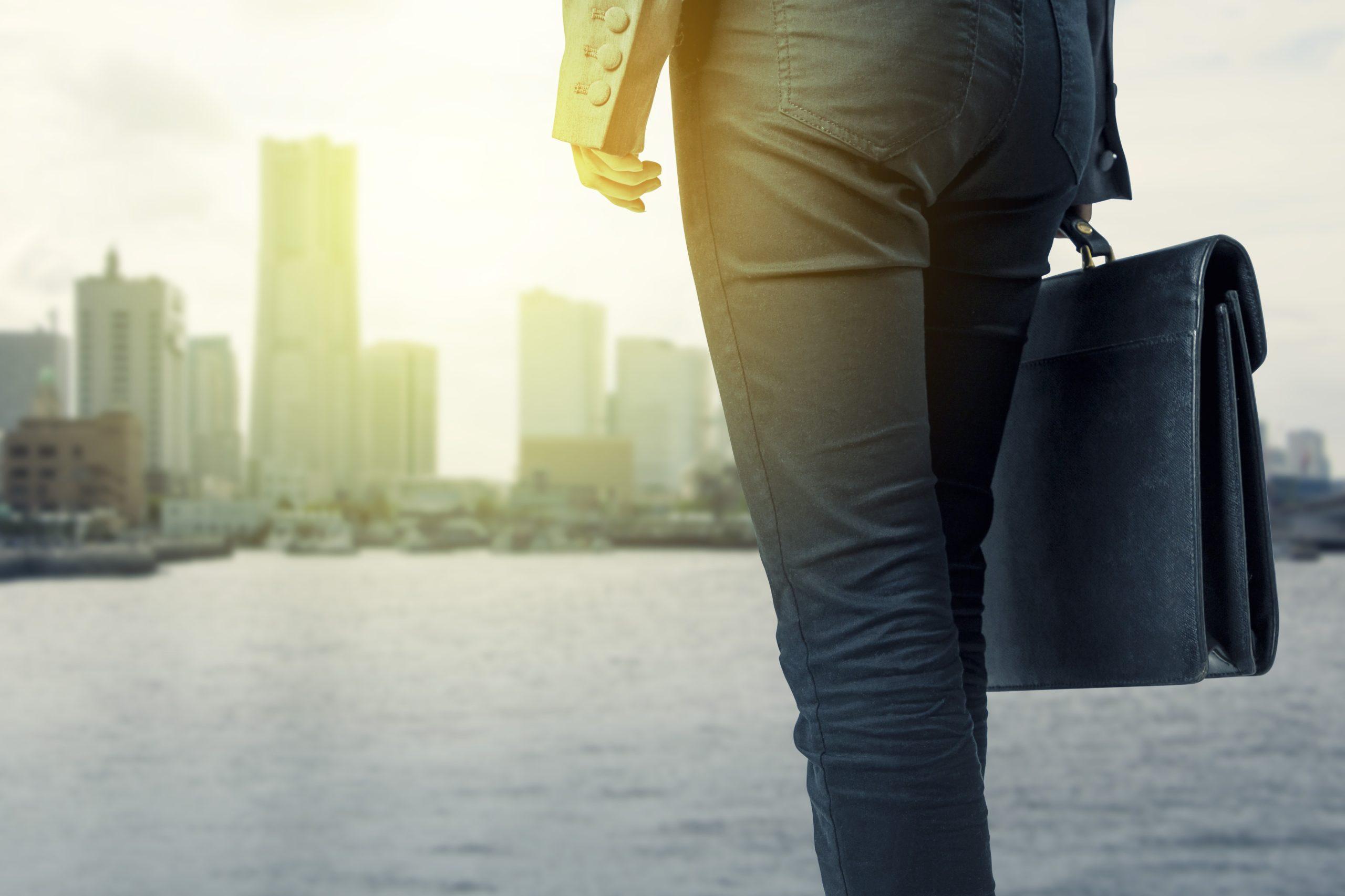 Close up of a person holding a briefcase in front of a harbor with a city in the background