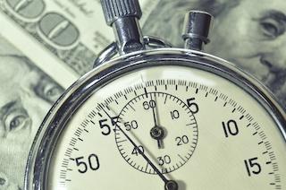 Close up of a pocket watch laying on top of one hundred dollar bills