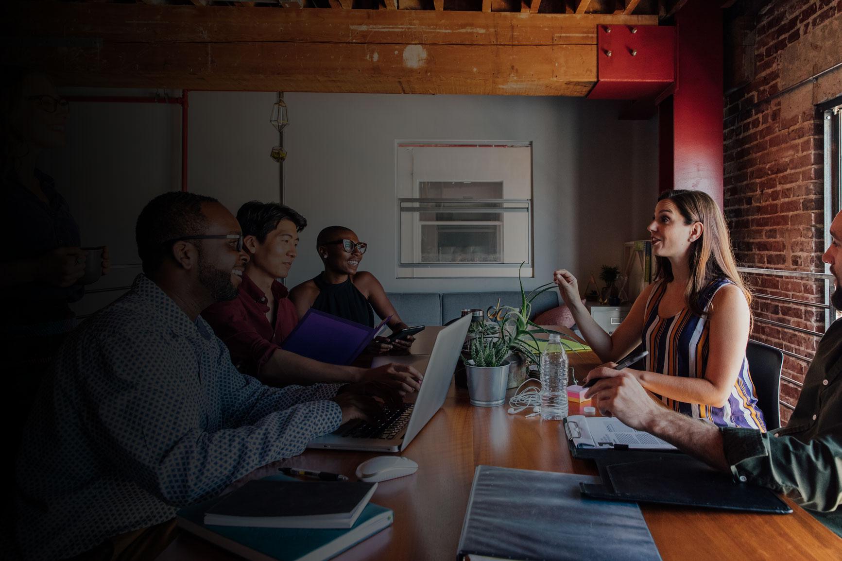 Photo of a woman leading a meeting at a communal table in a modern office